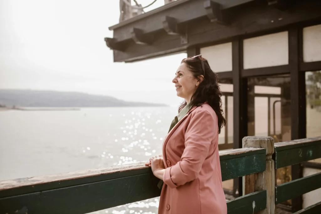 A happy woman standing by the water, symbolising the benefits of hormonal balance and natural health support through naturopathy